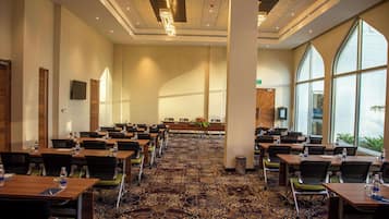 A conference room with multiple tables and chairs, a carpeted floor, and large windows.