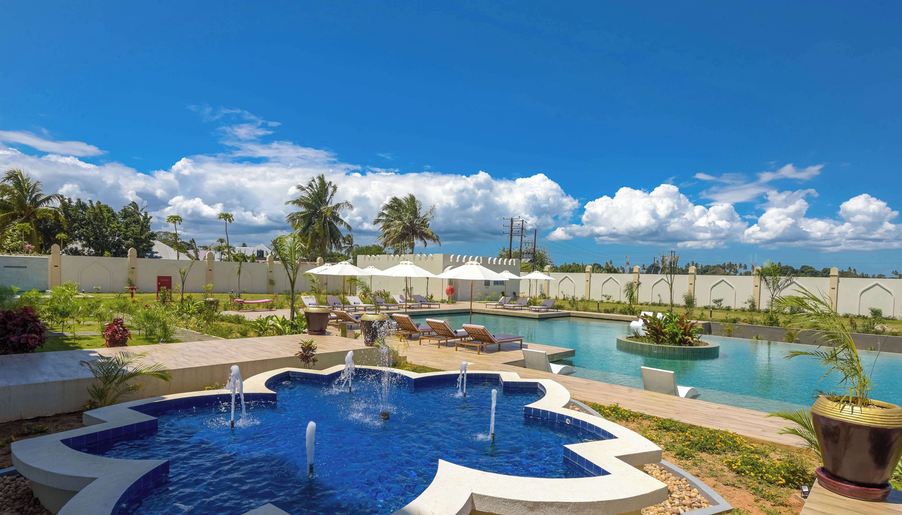 Un espace piscine comprenant plusieurs piscines, des chaises longues et des parasols.