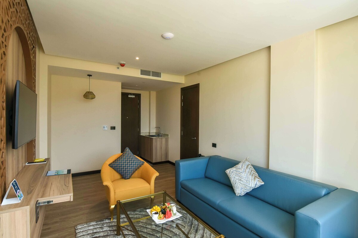 A modern living room with a blue sofa, yellow armchair, and a coffee table with fruit.