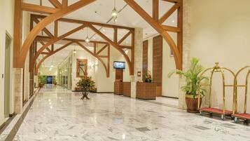 A spacious lobby with marble flooring, wooden beams, a reception desk, potted plants, and a television.