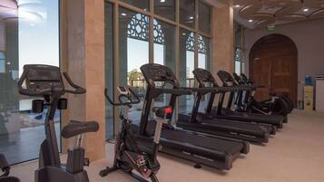 A row of stationary bikes and treadmills in a well-lit indoor area with large windows and a modern ceiling design.