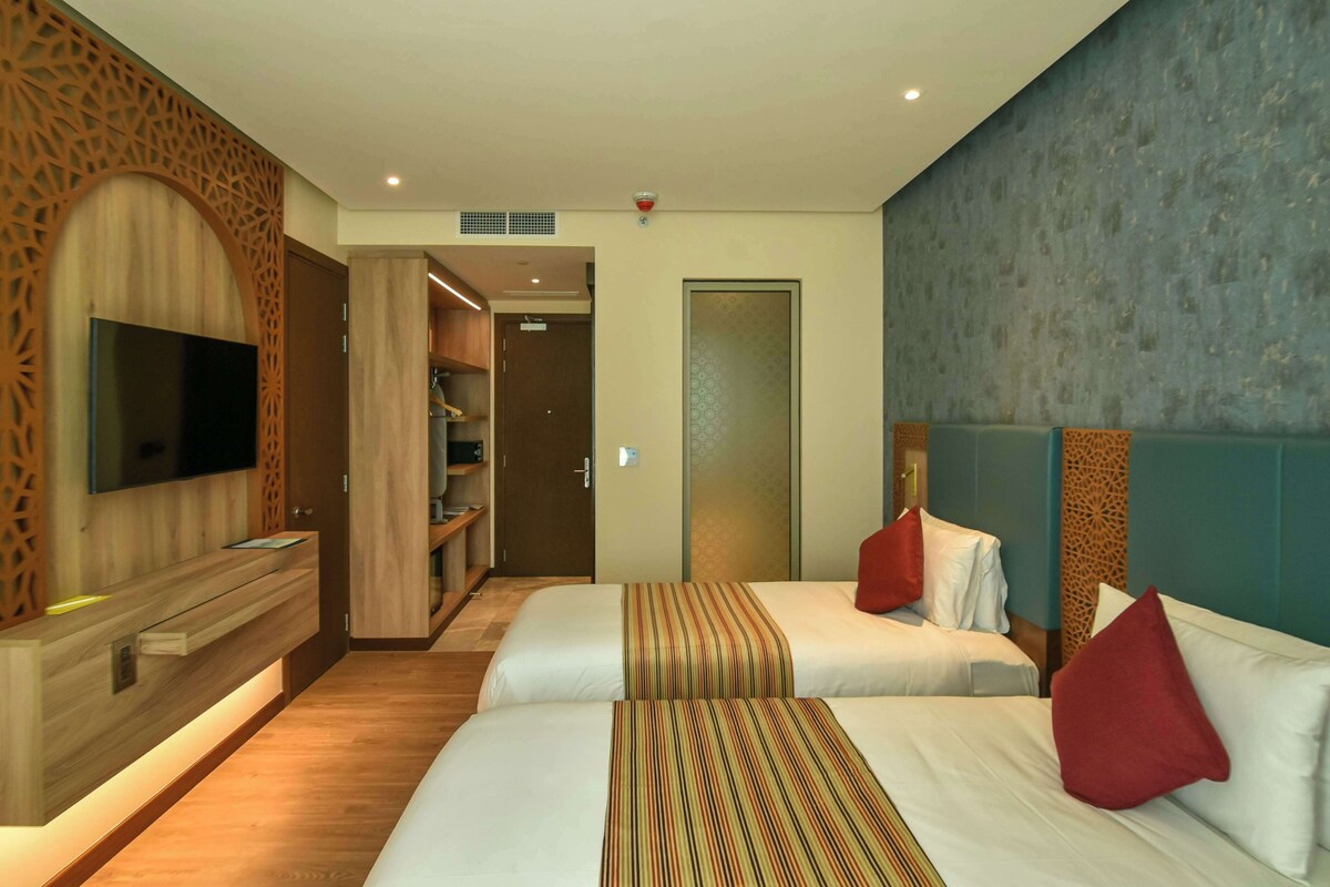 A hotel room with two beds, a flat-screen TV, a wooden console, and a wardrobe.