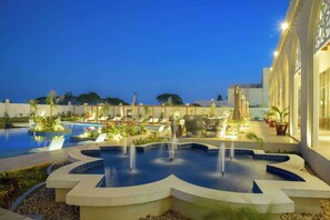 A pool area with a central fountain, surrounded by lounge chairs and potted plants. - Golden Tulip Zanzibar Airport (Zanzibar Town)