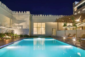A swimming pool with lounge chairs and umbrellas, surrounded by a white building with a high wall and a balcony. - Golden Tulip Zanzibar Airport (Zanzibar Town)