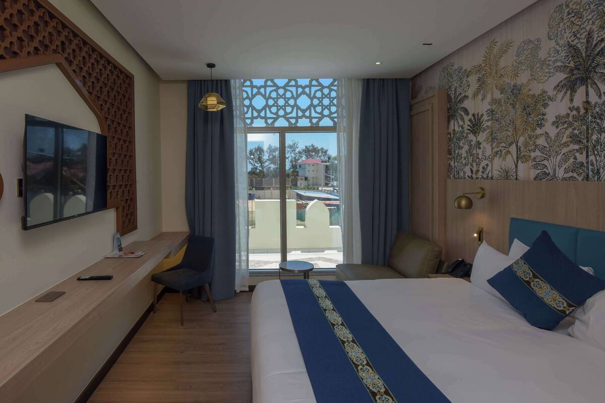 A hotel room with a large bed, a desk with a chair, a TV, and a view of the outside.