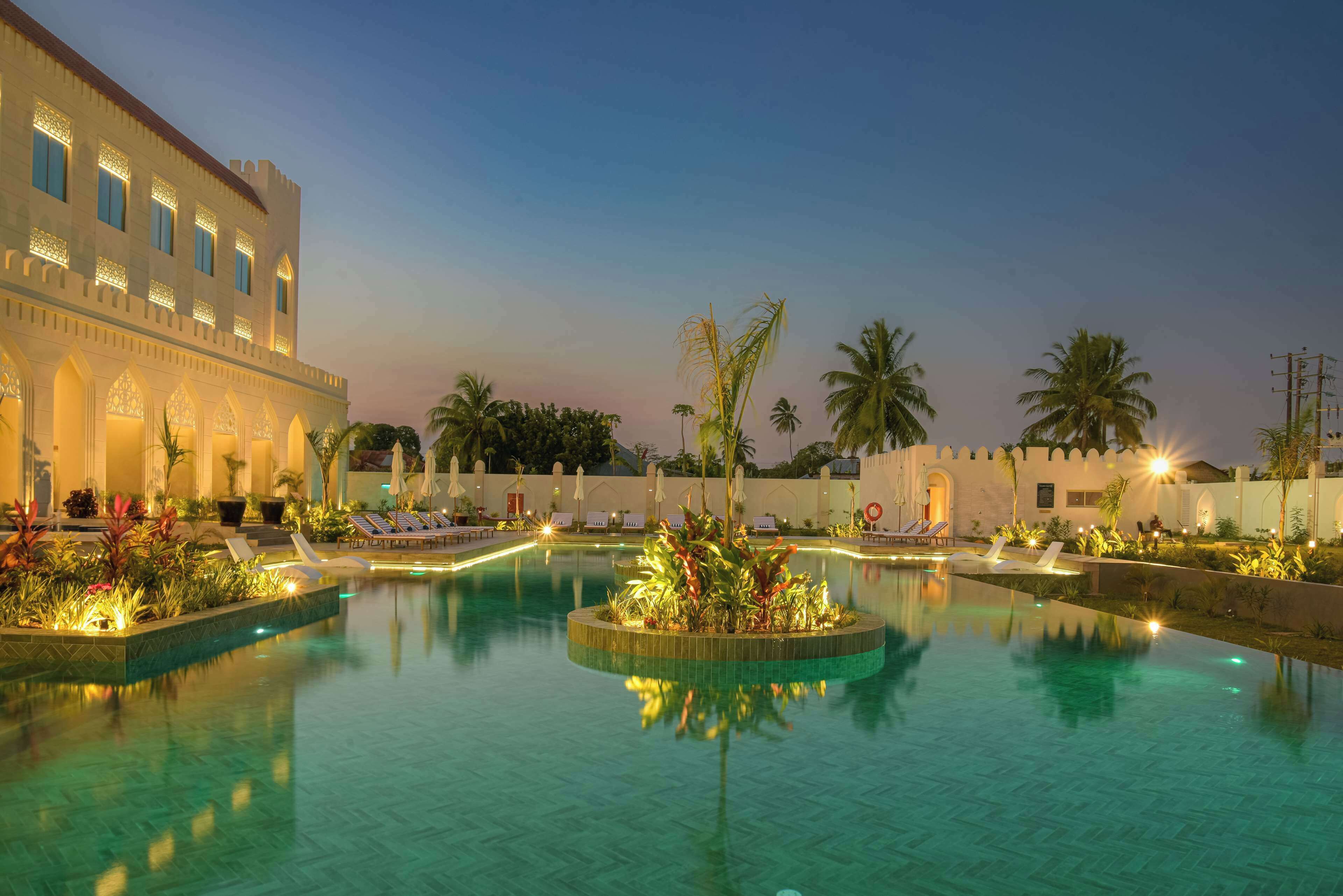 A hotel pool area with a large pool, palm trees, and lounge chairs.