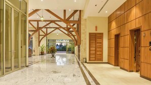 Vestíbulo de hotel con suelo de mármol, vigas de madera, una recepción y una puerta grande de madera.