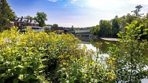 A riverside view with buildings, greenery, and a bridge. - Vermont get-away end unit townhouse nestled in the trees  (Hartford)