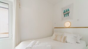 A neatly made bed with white linens and towels, a round wall-mounted light, and a framed picture on the wall. - Le Pitchoun - One Bedroom Apartment, Sleeps 2 (Marseille)