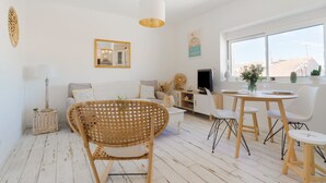 A bright, modern living room with a sofa, wicker chairs, a dining table, and a large window offering a view of the city. - Le Pitchoun - One Bedroom Apartment, Sleeps 2 (Marseille)