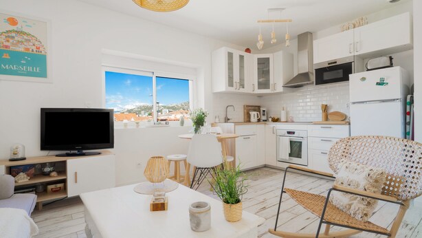 A modern kitchen with white cabinets, a built-in oven, and a microwave. There is a dining area with a table and chairs, and a television on a stand. - Le Pitchoun - One Bedroom Apartment, Sleeps 2 (Marseille)