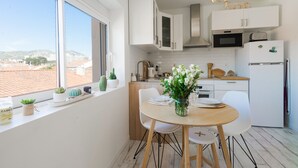 A modern kitchen with white cabinets, a dining table with chairs, and a view of the city through large windows. - Le Pitchoun - One Bedroom Apartment, Sleeps 2 (Marseille)