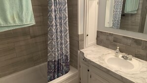 A bathroom with a bathtub, a sink with a marble countertop, and a shower curtain with a geometric pattern.
