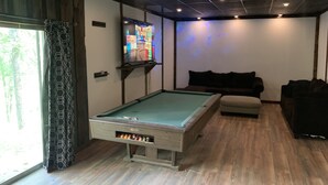 A pool table in a room with a wooden floor, a sofa, and a projector screen displaying a colorful image.