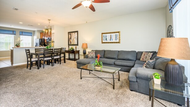 A modern living room with a gray sofa, a glass coffee table, and a dining area with a wooden table and chairs. - NEW Listing Beautiful Townhome CDC Compliant 4014 (Orlando)