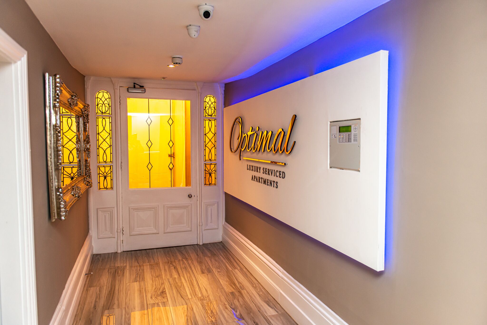 Un pasillo con un cartel que dice "Optimal Luxury Serviced Apartments" y una cámara de seguridad moderna en el techo.
