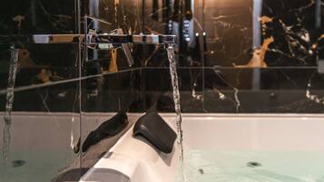 Eine Wanne mit fließendem Wasser, eine schwarze Badmatte und eine Wand mit Marmorplatten.