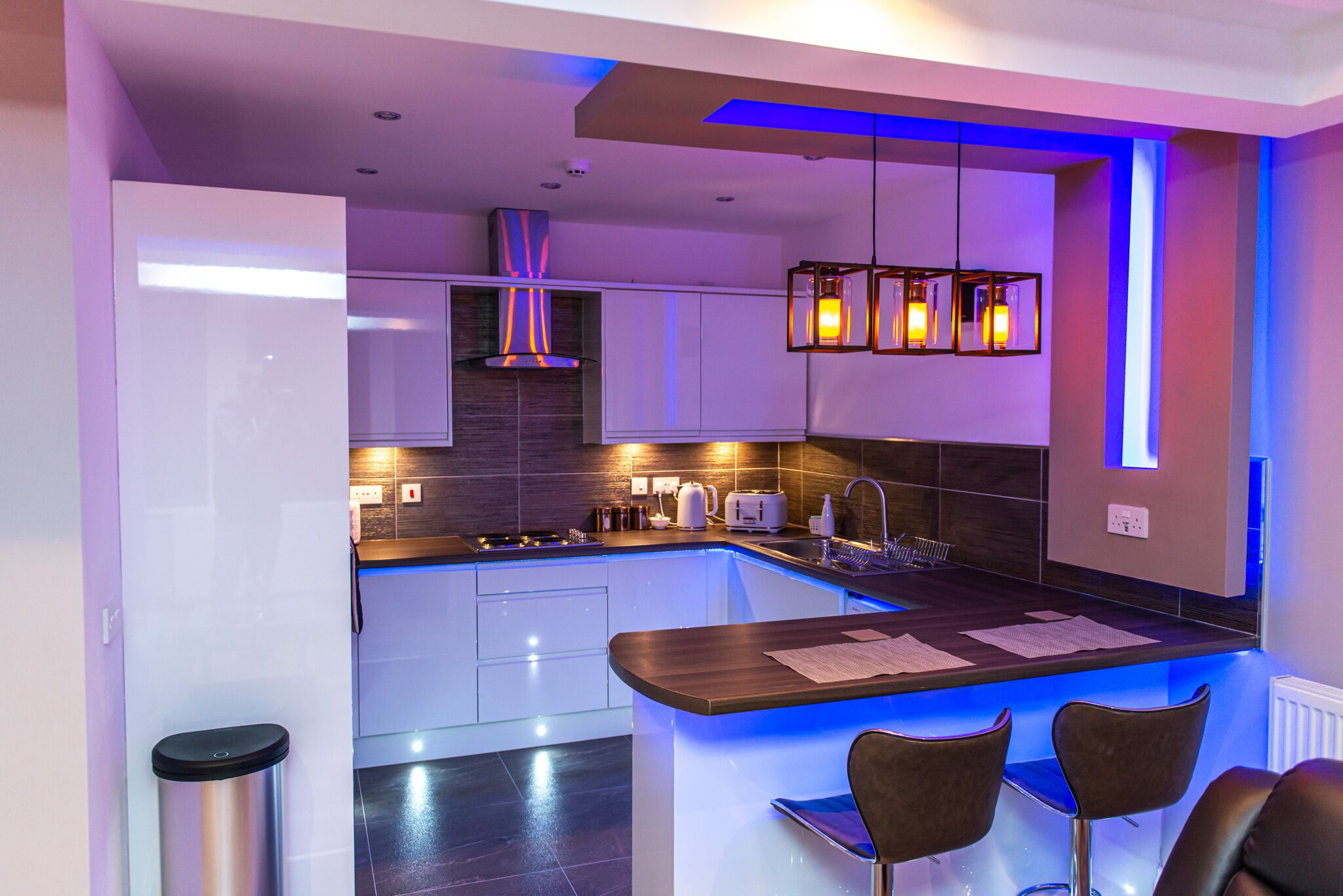 Une cuisine moderne dotée d’un îlot central, de meubles blancs et d’un éclairage d’ambiance bleu.