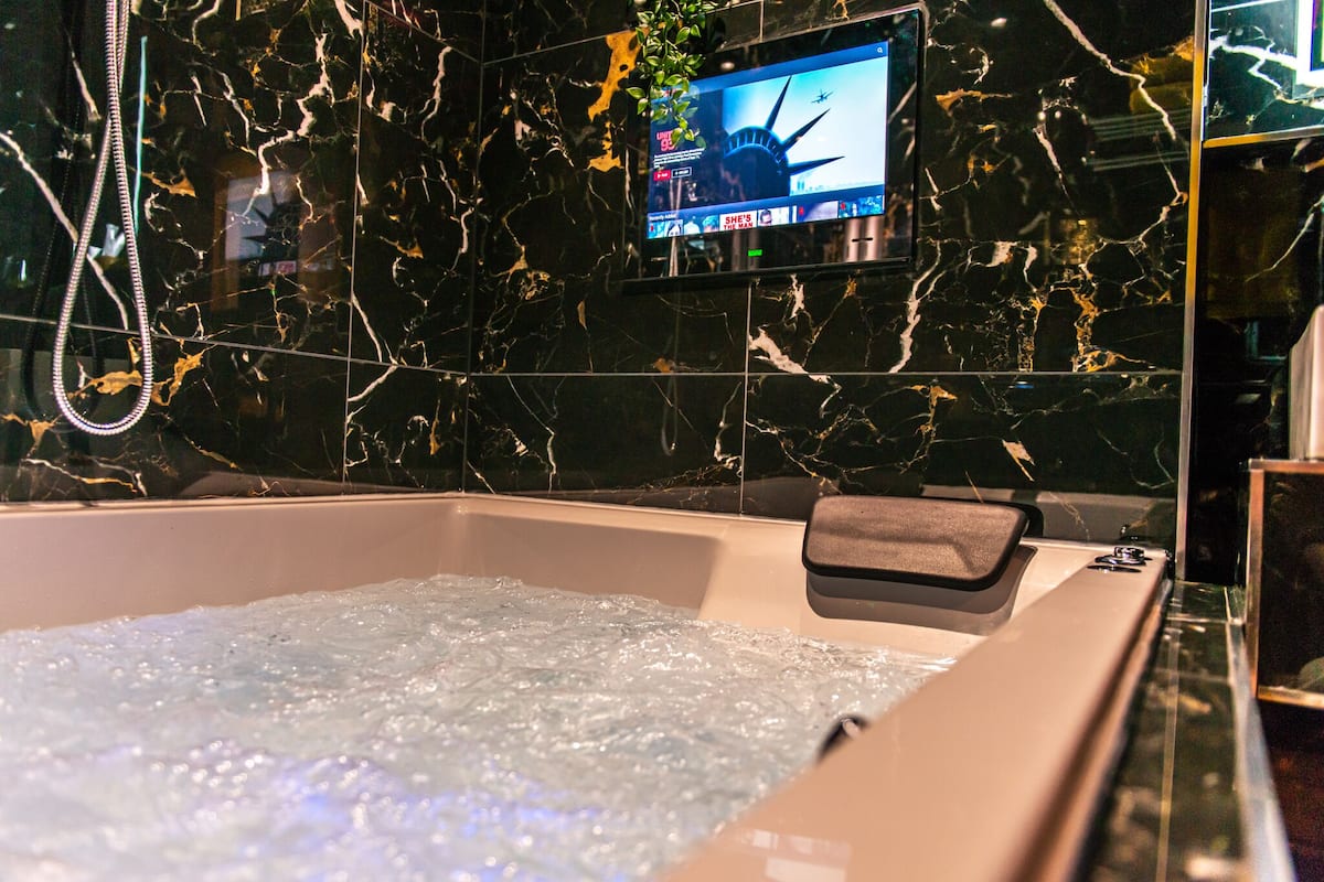 A modern bathroom with a marble wall, a television mounted above a bathtub, and a handheld showerhead.