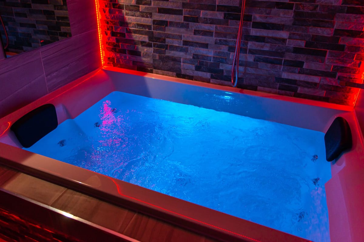 A rectangular hot tub with a brick wall backdrop and red lighting.