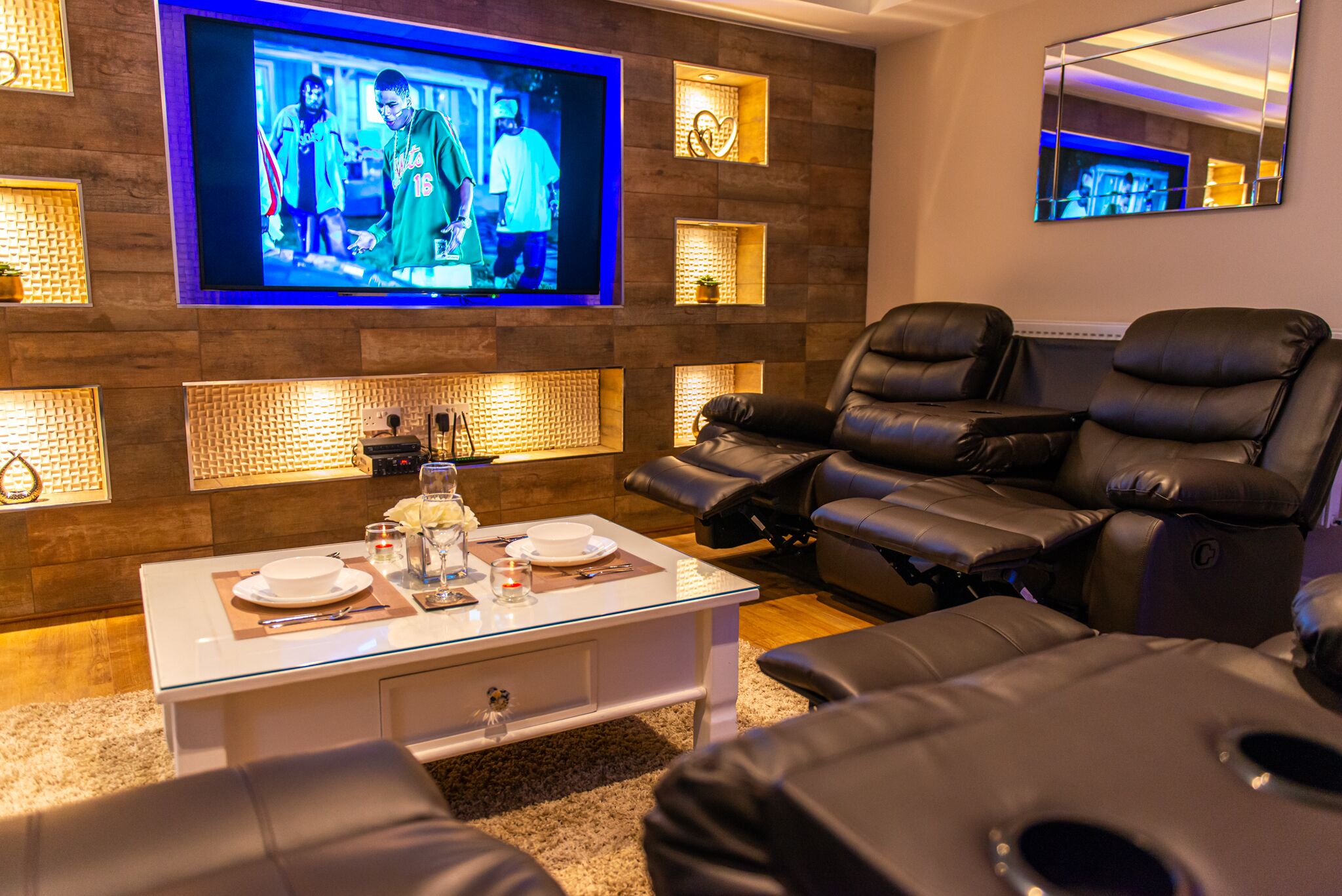 A modern living room with a flat-screen TV, leather recliners, and a coffee table with a white plate and glass.