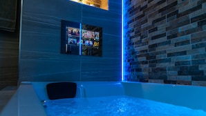 A modern bathroom with a bathtub, a wall-mounted digital screen displaying various content, and a brick accent wall.