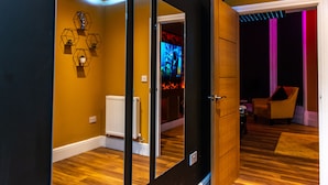 A room with a wooden floor, a radiator, and a mirror reflecting a TV screen.