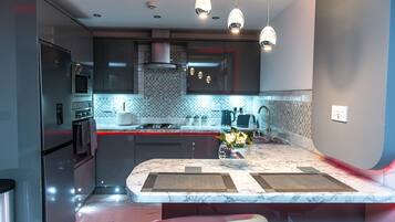 Una cocina moderna con encimera de mármol, electrodomésticos de acero inoxidable, iluminación colgante y una isla central con taburetes.