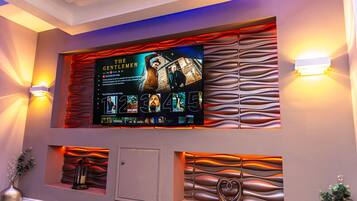Pared con un televisor montado mostrando la película 'The Gentleman', paneles decorativos y dos lámparas de pared.