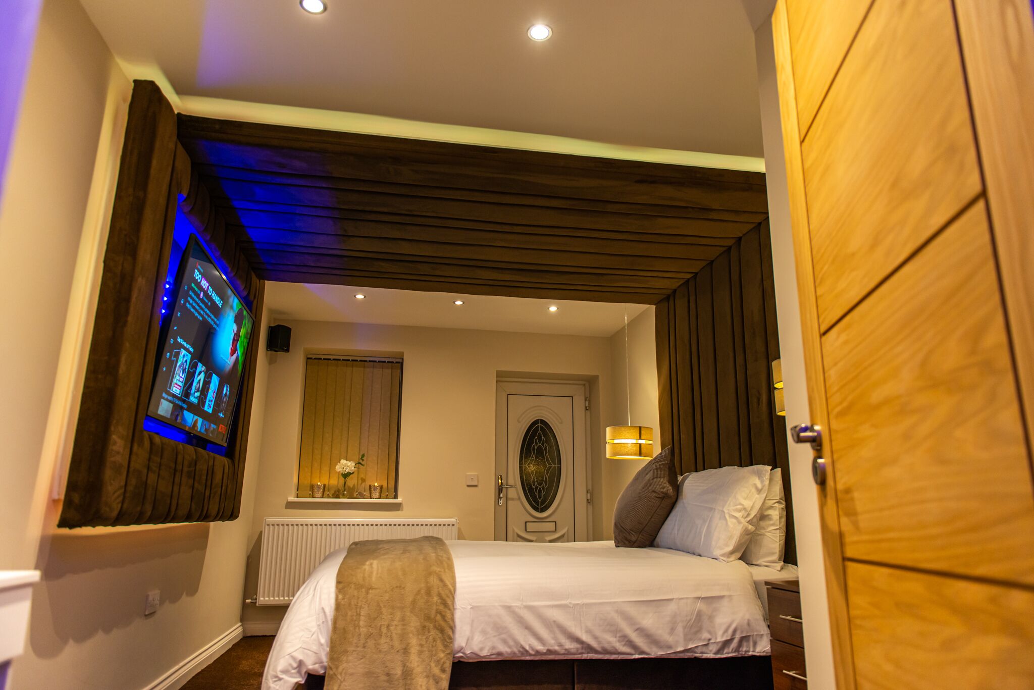 Une chambre à coucher avec un lit, une armoire en bois, un téléviseur fixé au mur et une fenêtre avec des rideaux.