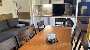 Un espacio habitable compacto con sofá, mesa de comedor, sillas, lavadora y zona de cocina.