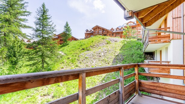 Un balcon en bois offrant une vue sur une colline et des bâtiments.
