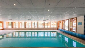 Une piscine intérieure avec un sol carrelé, de grandes fenêtres et un banc le long du mur.