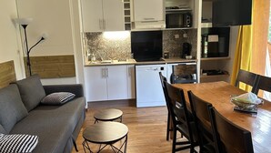 Un espace de vie compact comprenant un canapé, une table à manger, des chaises, un coin cuisine équipé d’appareils électroménagers et un téléviseur.