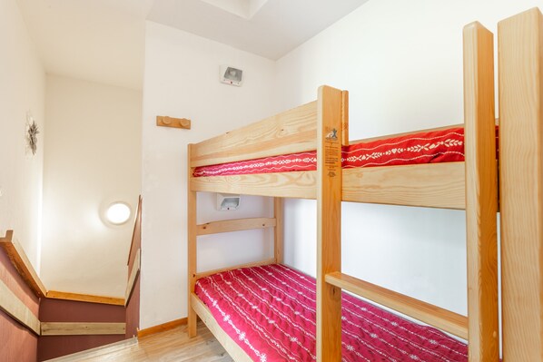 A bunk bed with a red patterned bedspread, a wooden headboard, and a small shelf.