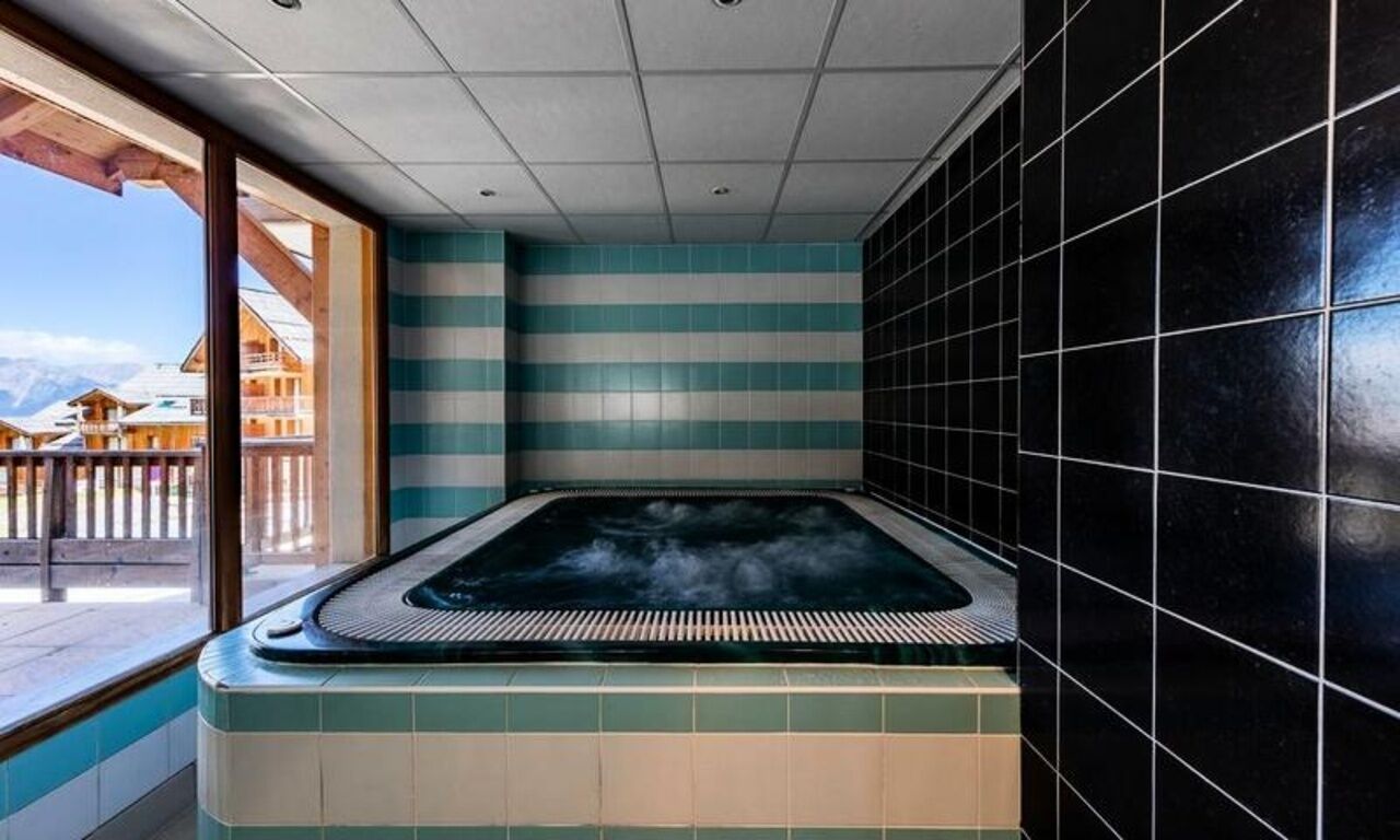 A hot tub with a view of mountains, a tiled wall, and a wooden deck.
