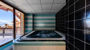 Un bain à remous avec vue sur les montagnes, un mur carrelé et une terrasse en bois.