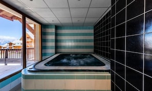 Un jacuzzi con vistas a montañas, una pared de azulejos y una terraza de madera.