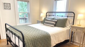 A neatly made bed with a green blanket, two bedside lamps, and a window with blinds. - Classic brick charmer close to lake, river, and downtown! (Sheboygan)