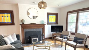 A living room with a fireplace, a television, and two armchairs. - Classic brick charmer close to lake, river, and downtown! (Sheboygan)