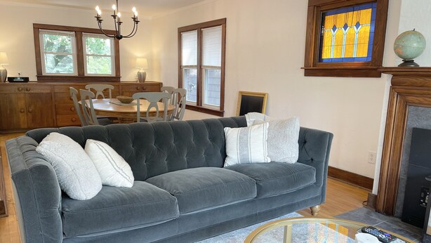 A living room with a dark grey sofa, a glass coffee table, and a chandelier. - Classic brick charmer close to lake, river, and downtown! (Sheboygan)