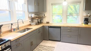 A modern kitchen with grey cabinets, a dishwasher, a stove, and a coffee maker. - Classic brick charmer close to lake, river, and downtown! (Sheboygan)