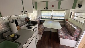 A compact RV kitchen with a gas stove, sink, and a small dining area with a bench. - “Maybelline”, 1959 Vintage Camper by the Creek (Barnardsville)