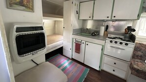 A compact kitchenette with a stove, sink, and a small refrigerator. - “Maybelline”, 1959 Vintage Camper by the Creek (Barnardsville)