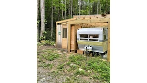 A small wooden cabin with a metal trailer attached, surrounded by a forest. - “Maybelline”, 1959 Vintage Camper by the Creek (Barnardsville)