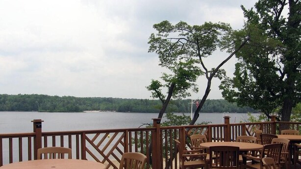 A wooden deck with tables and chairs overlooking a lake.