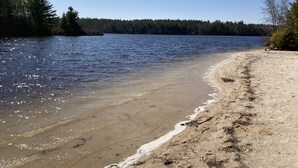 A beach with clear water and a forested shoreline.