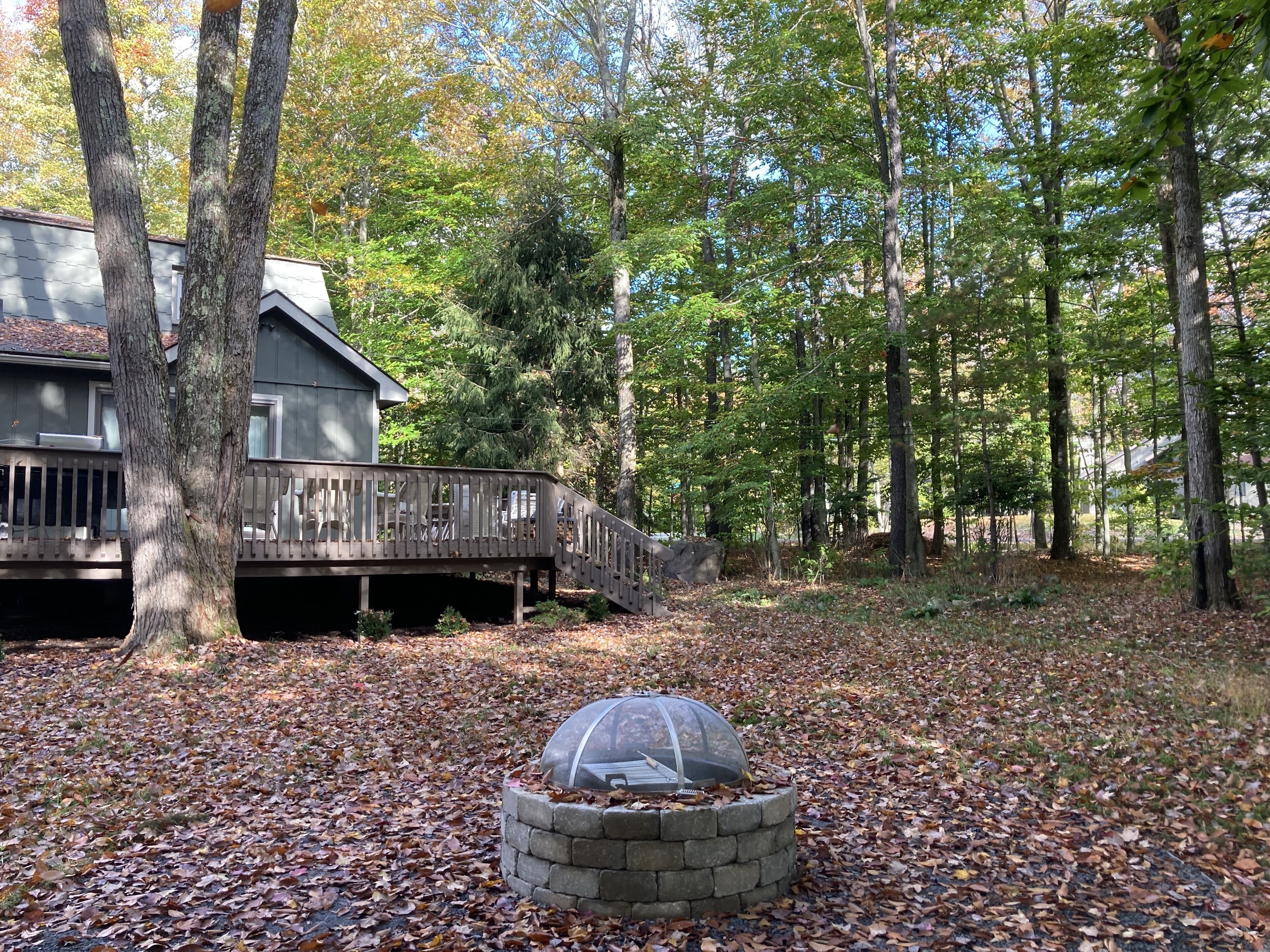 A cabin with a wooden deck and a stone fire pit surrounded by fallen leaves.
