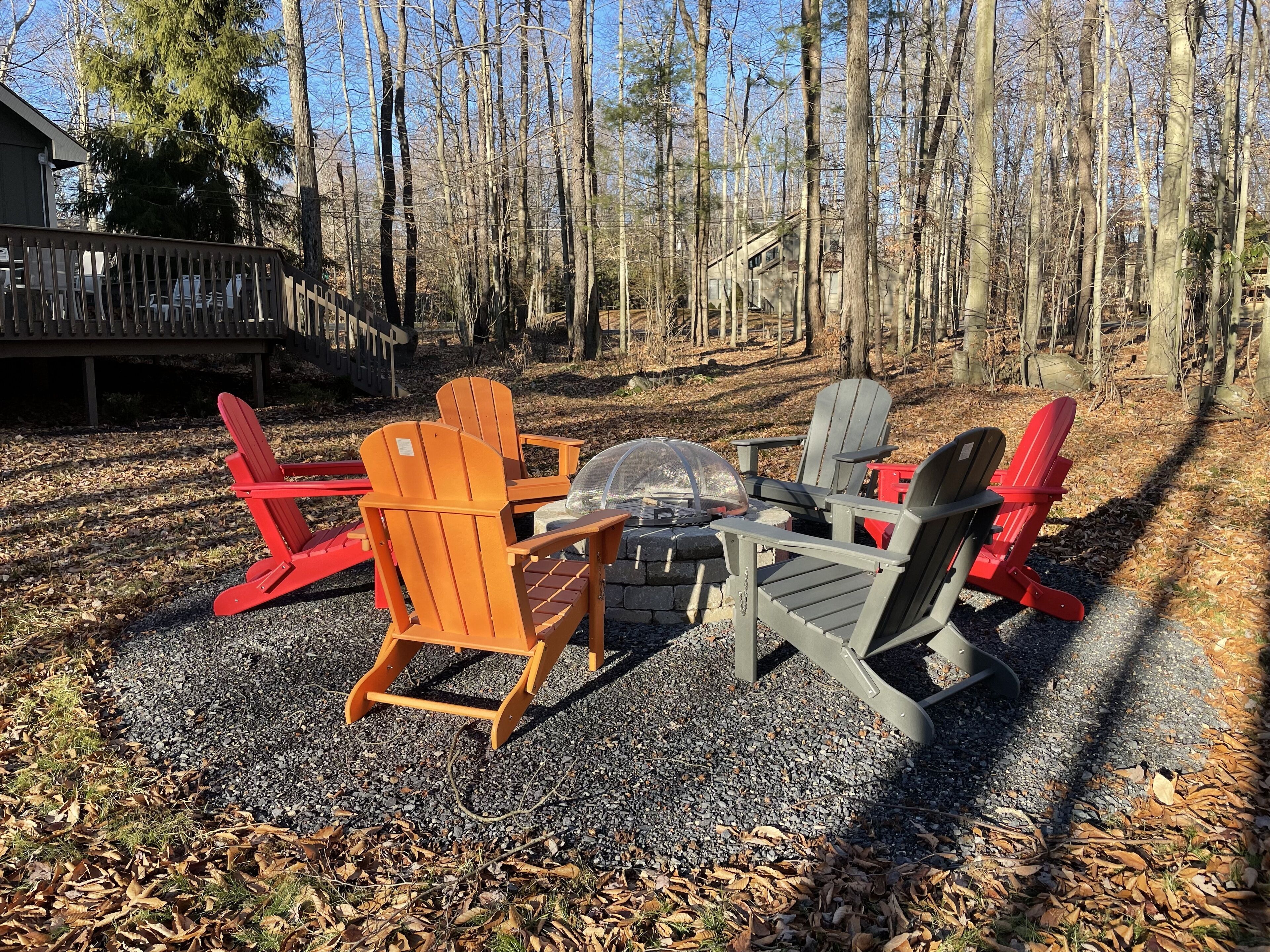 A fire pit surrounded by Adirondack chairs in a forest setting.