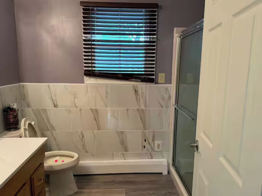 Une salle de bain avec une douche, des toilettes et une fenêtre équipée de stores.
